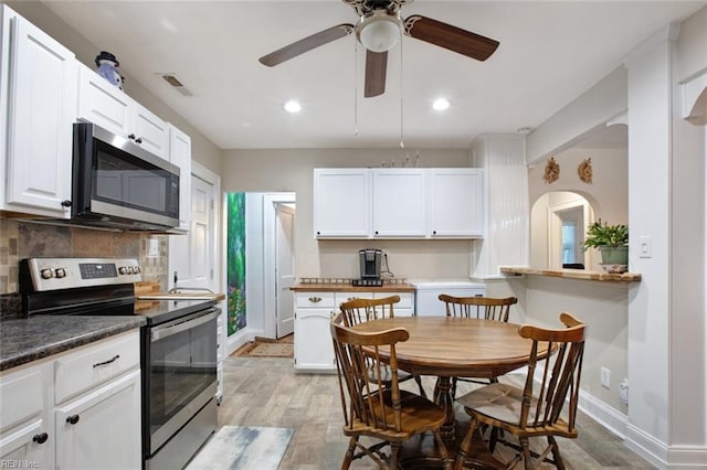 kitchen with visible vents, white cabinetry, stainless steel appliances, light wood-style floors, and decorative backsplash