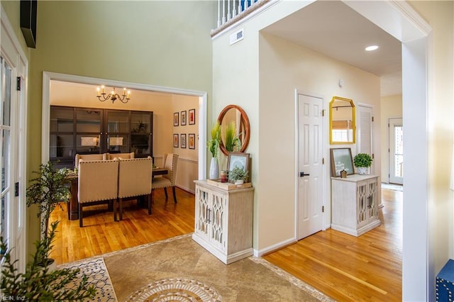 hallway with a high ceiling, wood finished floors, visible vents, and a chandelier