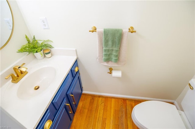 bathroom with vanity, toilet, wood finished floors, and baseboards