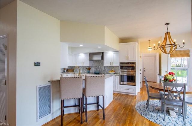 kitchen featuring visible vents, a breakfast bar, tasteful backsplash, double oven, and white cabinets