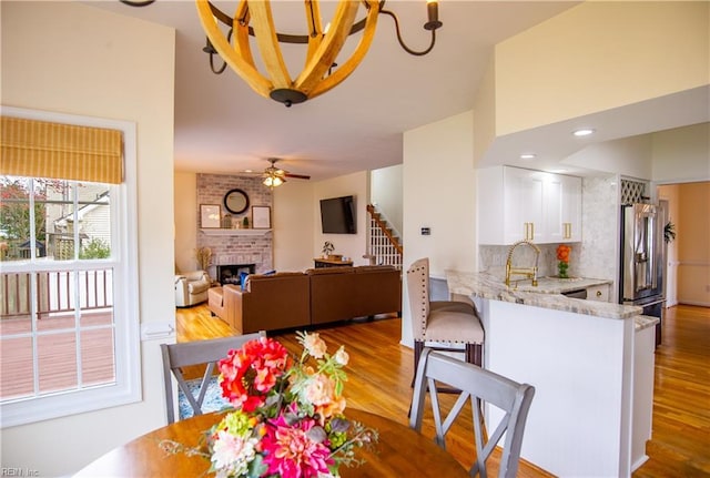 dining room featuring ceiling fan with notable chandelier, light wood-style flooring, stairs, and a fireplace