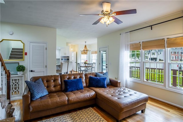 living area featuring stairs, ceiling fan with notable chandelier, and light wood-type flooring