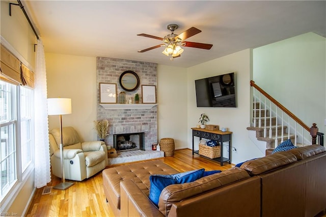 living room with wood finished floors, visible vents, ceiling fan, stairs, and a brick fireplace