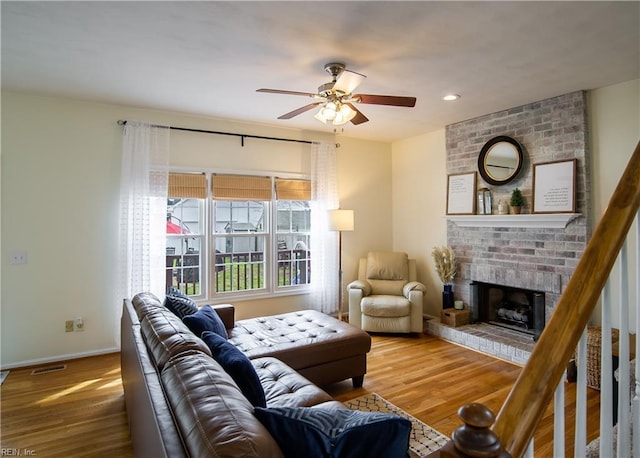 living room with baseboards, a brick fireplace, wood finished floors, and a ceiling fan