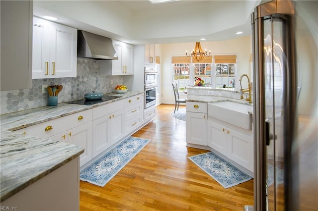 kitchen with light wood-style flooring, stainless steel appliances, white cabinetry, wall chimney exhaust hood, and a sink