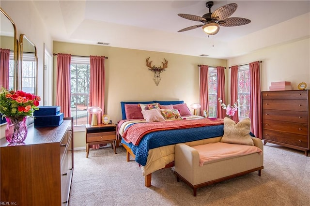 bedroom with visible vents, light colored carpet, a ceiling fan, and a tray ceiling