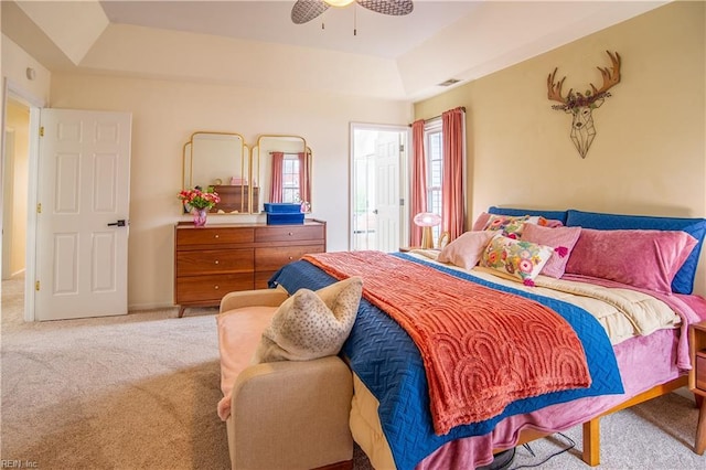 carpeted bedroom with a raised ceiling, visible vents, and ceiling fan