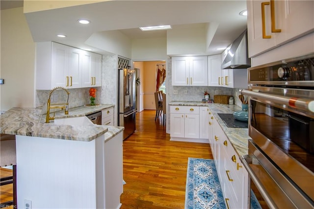 kitchen with wall chimney range hood, a breakfast bar area, light wood-style flooring, appliances with stainless steel finishes, and a peninsula