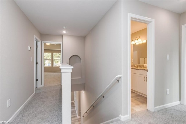 hall featuring an upstairs landing, light colored carpet, and baseboards