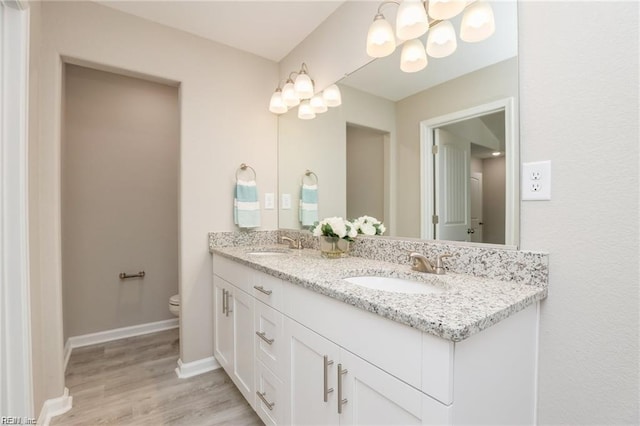 bathroom featuring baseboards, toilet, an inviting chandelier, and a sink