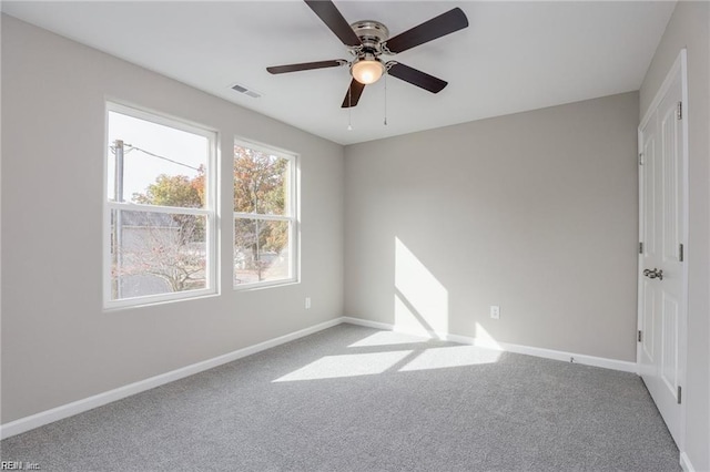 carpeted empty room with visible vents, baseboards, and a ceiling fan