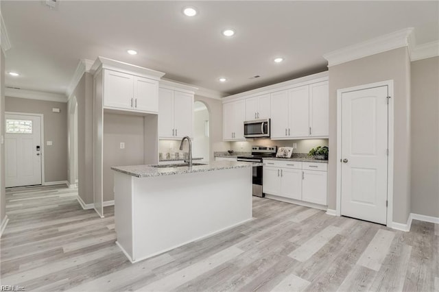 kitchen with arched walkways, a sink, ornamental molding, stainless steel appliances, and white cabinets