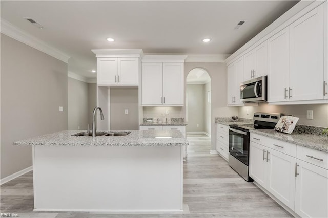 kitchen with an island with sink, ornamental molding, stainless steel appliances, white cabinetry, and a sink