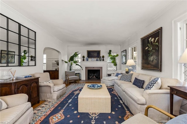 living area featuring arched walkways, a fireplace with flush hearth, crown molding, and wood finished floors