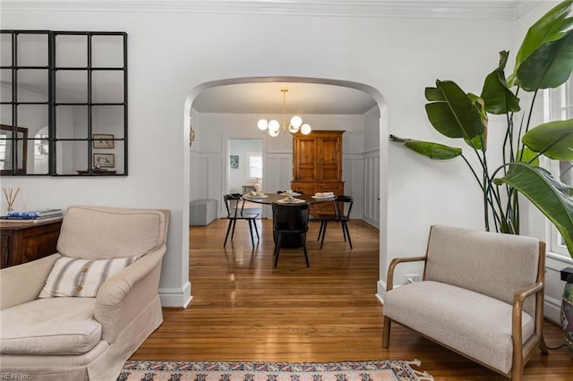 interior space featuring a notable chandelier, wood finished floors, arched walkways, and ornamental molding