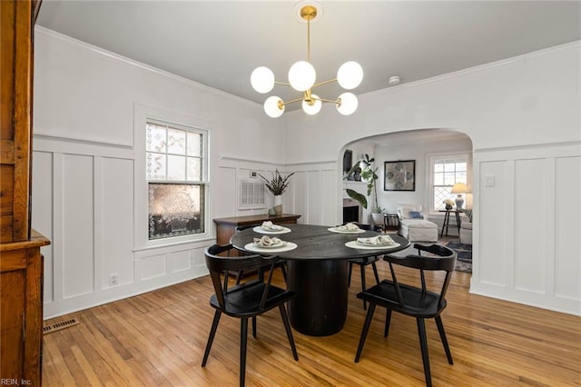 dining area featuring arched walkways, a decorative wall, light wood finished floors, and a chandelier