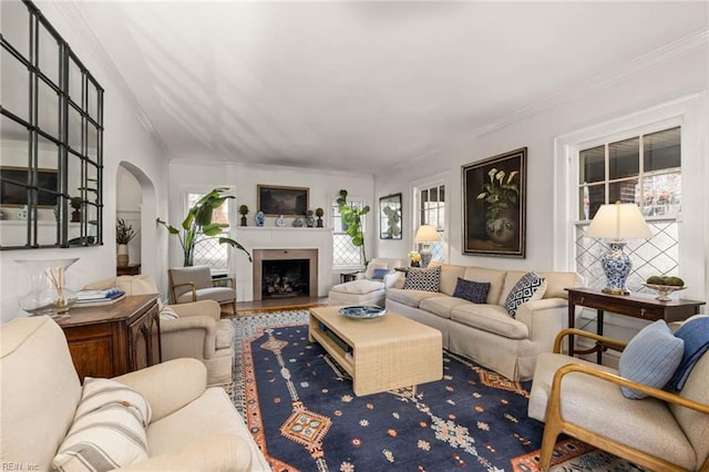 living area featuring wood finished floors, arched walkways, ornamental molding, and a fireplace