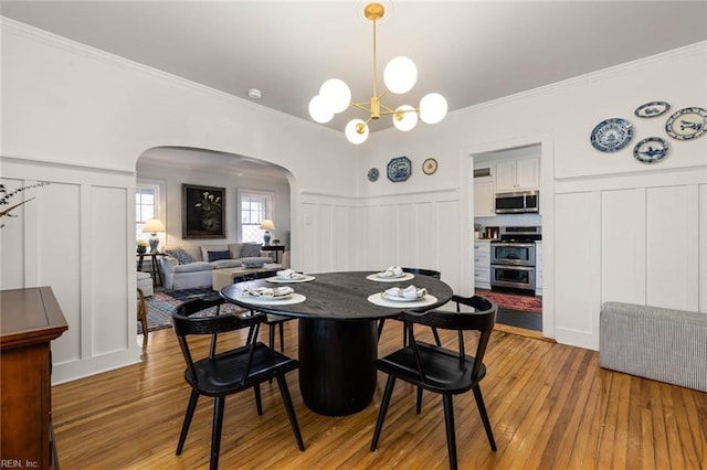 dining space with a notable chandelier, arched walkways, light wood-style floors, and a decorative wall