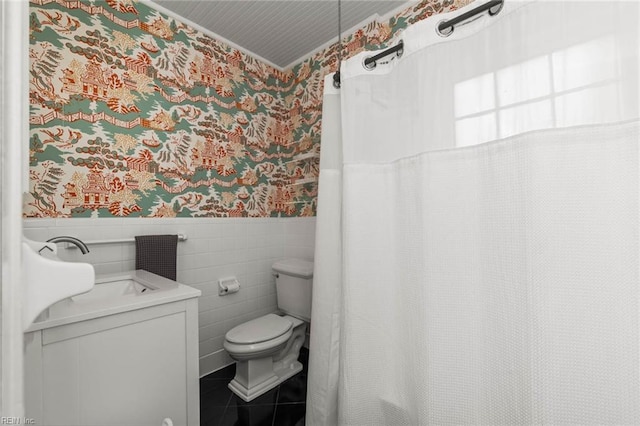 full bathroom featuring a wainscoted wall, wallpapered walls, tile patterned floors, toilet, and tile walls