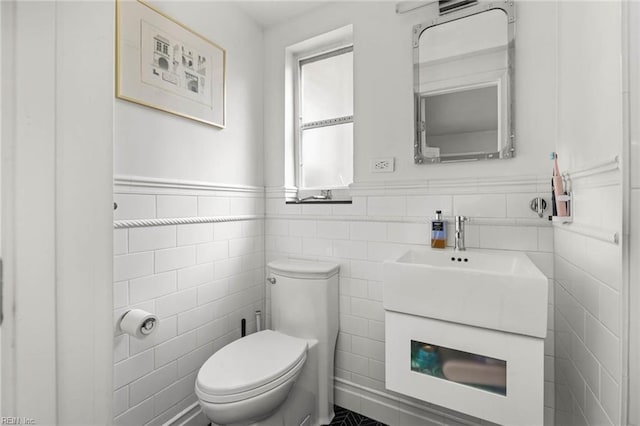 half bath featuring vanity, tile walls, toilet, and a wainscoted wall