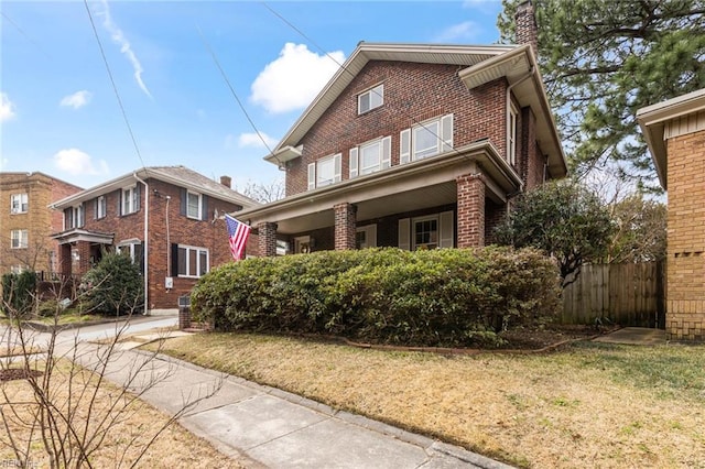 traditional home with brick siding, a chimney, a front lawn, and fence