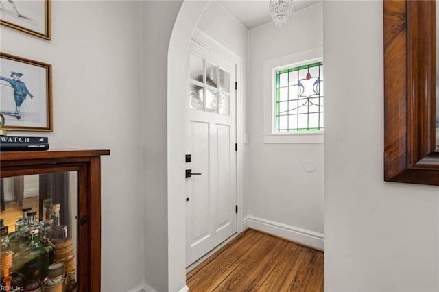 doorway to outside with wood finished floors, arched walkways, and baseboards