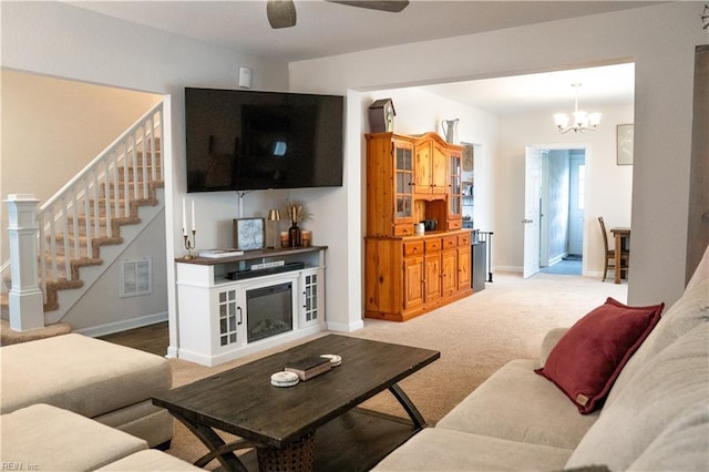 living area featuring visible vents, baseboards, light colored carpet, stairs, and ceiling fan with notable chandelier