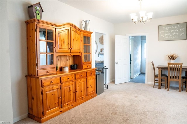 kitchen with brown cabinetry, baseboards, glass insert cabinets, light colored carpet, and a chandelier