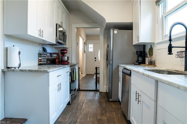 kitchen featuring light stone counters, dark wood-style flooring, a sink, appliances with stainless steel finishes, and white cabinetry