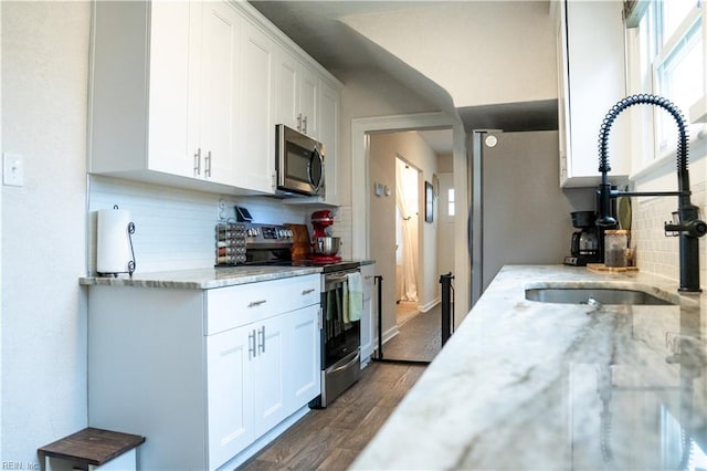 kitchen featuring dark wood-type flooring, light stone counters, appliances with stainless steel finishes, white cabinetry, and a sink