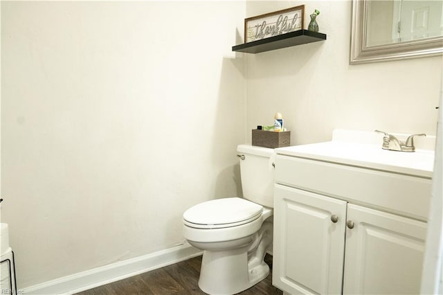 half bath with toilet, vanity, baseboards, and wood finished floors