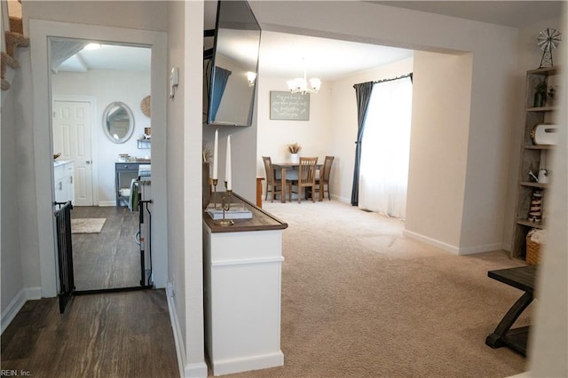 hall featuring baseboards, carpet floors, and an inviting chandelier