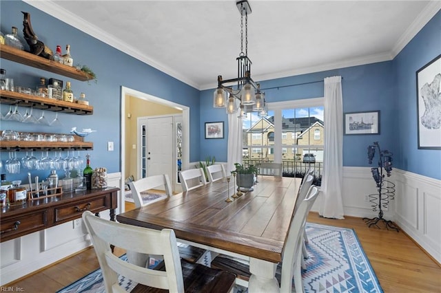 dining space featuring light wood-style floors, a chandelier, wainscoting, and crown molding