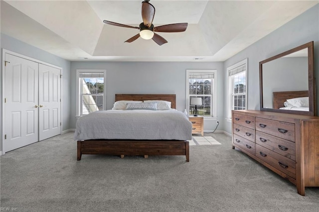 bedroom featuring light colored carpet, baseboards, a tray ceiling, and ceiling fan