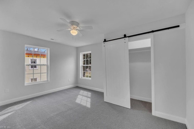 unfurnished bedroom with visible vents, a barn door, carpet, baseboards, and ceiling fan