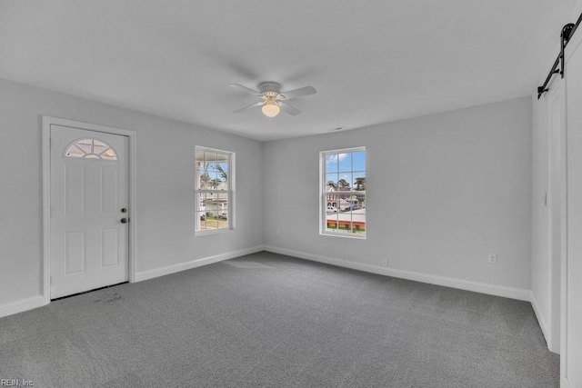 foyer featuring a barn door, carpet flooring, baseboards, and ceiling fan