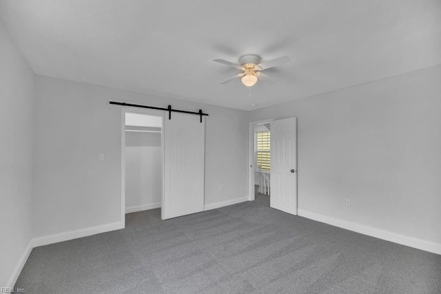 unfurnished bedroom featuring dark carpet, baseboards, a barn door, and ceiling fan