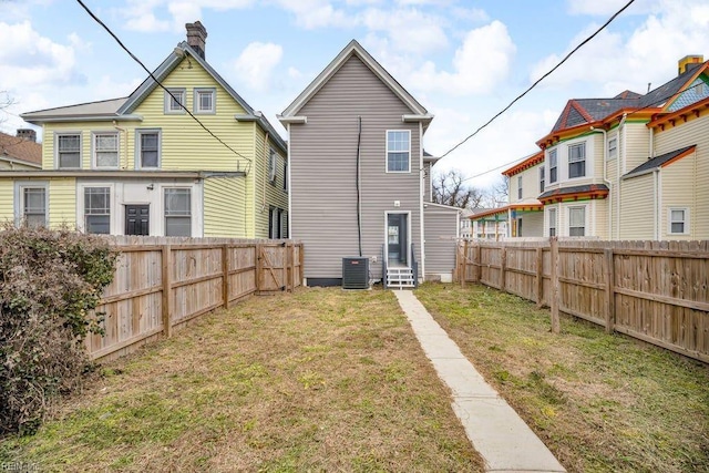 rear view of house with entry steps, a yard, a fenced backyard, and central AC