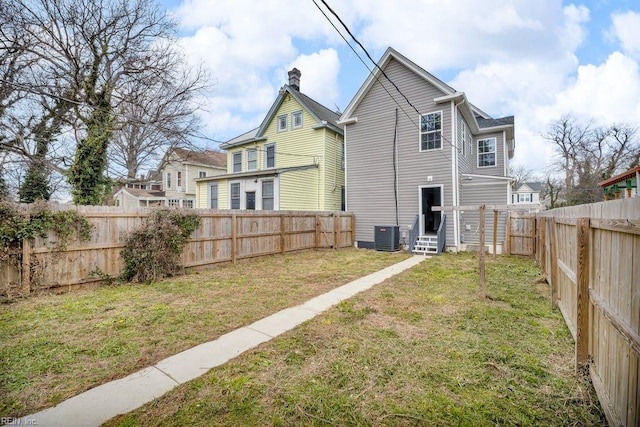 rear view of property featuring a yard, a fenced backyard, a chimney, and entry steps