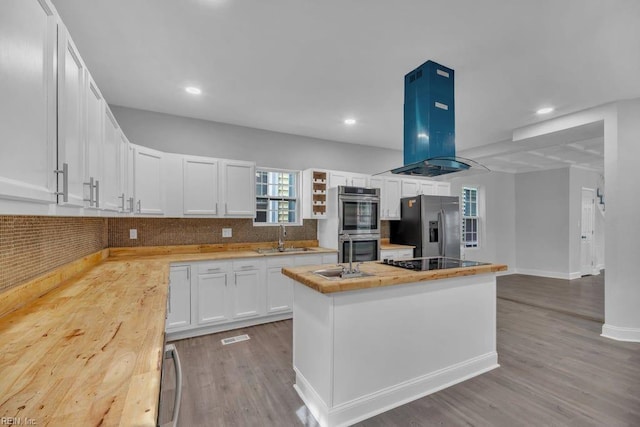 kitchen with butcher block countertops, island exhaust hood, a sink, a center island, and appliances with stainless steel finishes