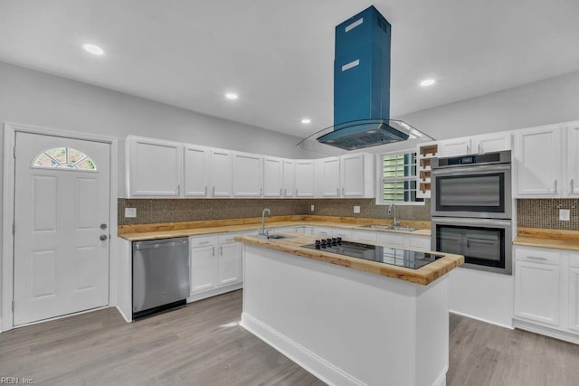 kitchen with light wood-type flooring, island exhaust hood, stainless steel appliances, white cabinetry, and a sink