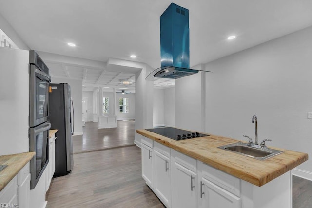 kitchen featuring black appliances, butcher block countertops, a sink, island exhaust hood, and light wood finished floors