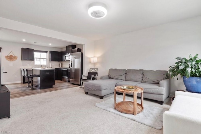 living area with light carpet, recessed lighting, light wood-style floors, and baseboards