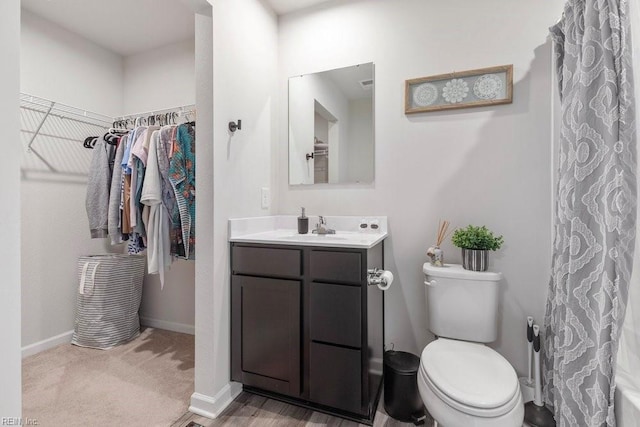 bathroom featuring a walk in closet, toilet, vanity, and baseboards