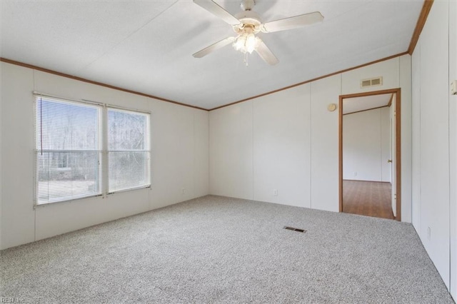 empty room with visible vents, a ceiling fan, ornamental molding, and carpet flooring