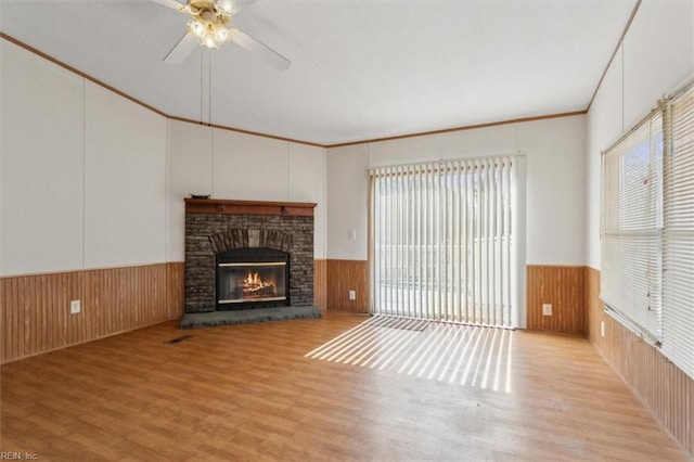 unfurnished living room featuring wood finished floors, wooden walls, a fireplace, and wainscoting