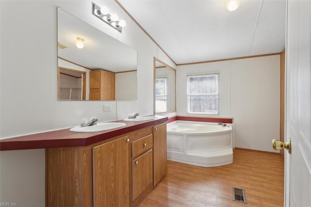 full bath with visible vents, a garden tub, lofted ceiling, wood finished floors, and a sink