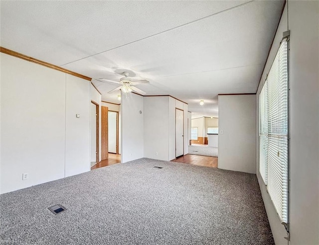 carpeted spare room featuring visible vents, a ceiling fan, crown molding, and a textured ceiling