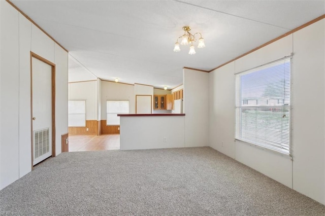 carpeted spare room with wooden walls, visible vents, crown molding, vaulted ceiling, and an inviting chandelier