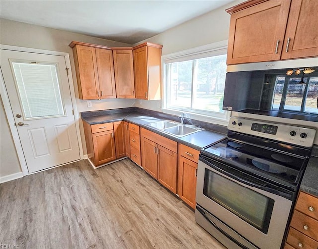 kitchen featuring brown cabinetry, light wood finished floors, a sink, stainless steel appliances, and dark countertops